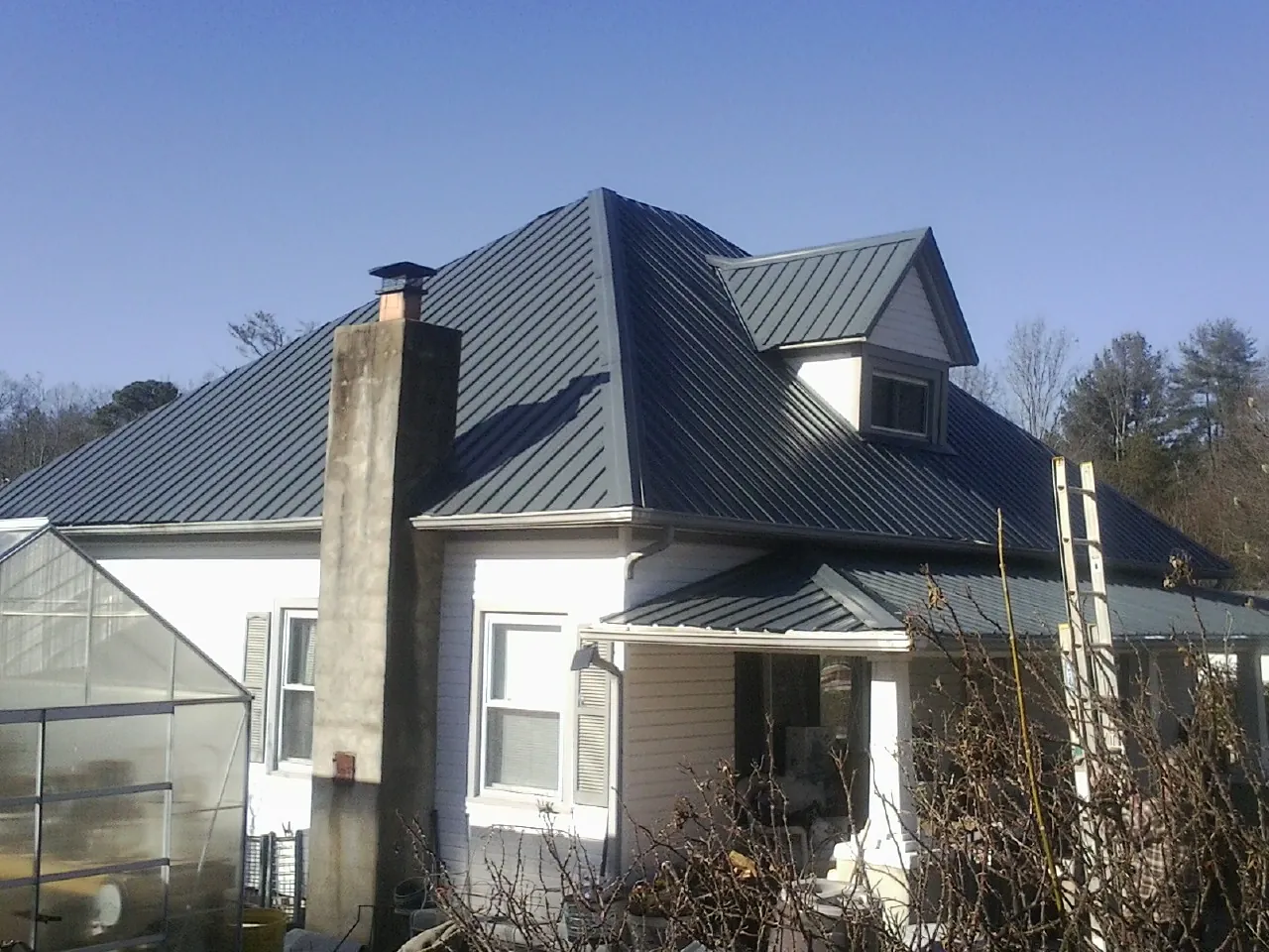 Dark blue standing seam metal roof on a white farmhouse with dormer — Slate & Tile Roof Repair by Roofing Brothers in Sherburne
