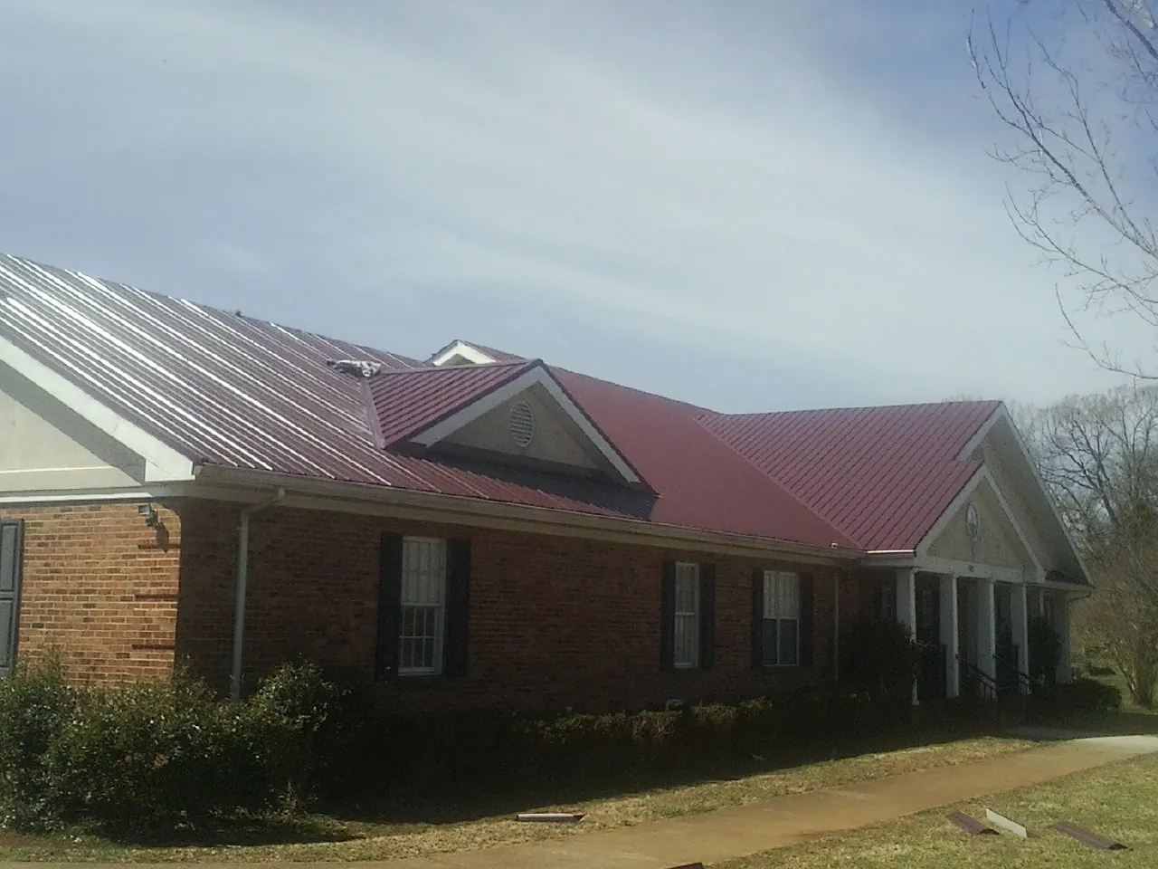 Red metal roof with gabled entries on a long brick building, from a Hail Damage Roof Repair job in Sherburne