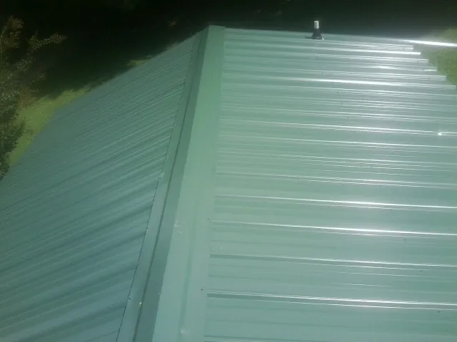 New green metal panels meeting at the ridge of a roof — Flat Roof Repair work by our crew in Sherburne