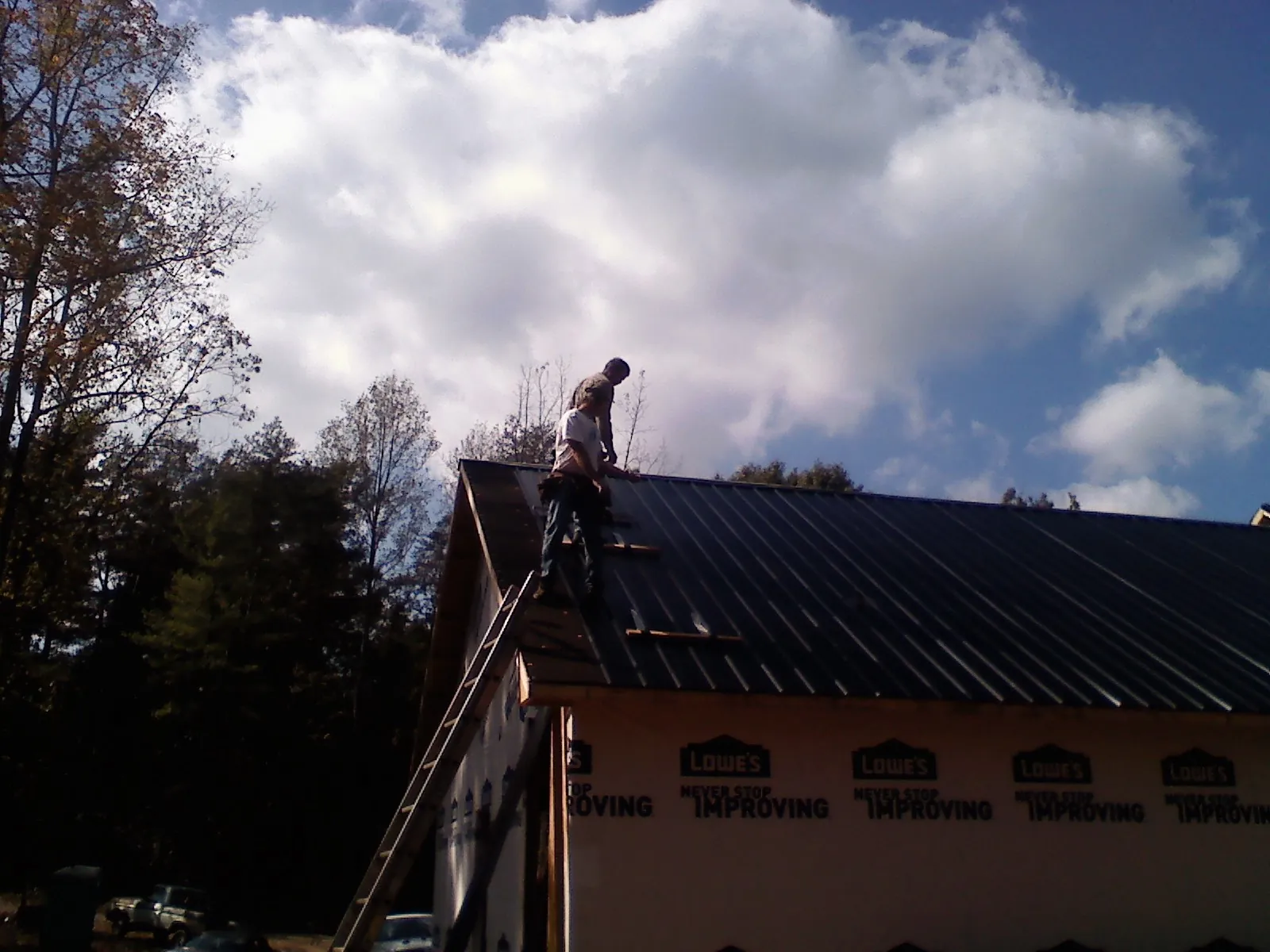 Roofer fastening dark metal panels high against a cloudy sky, from a Roof Inspection job in Sherburne
