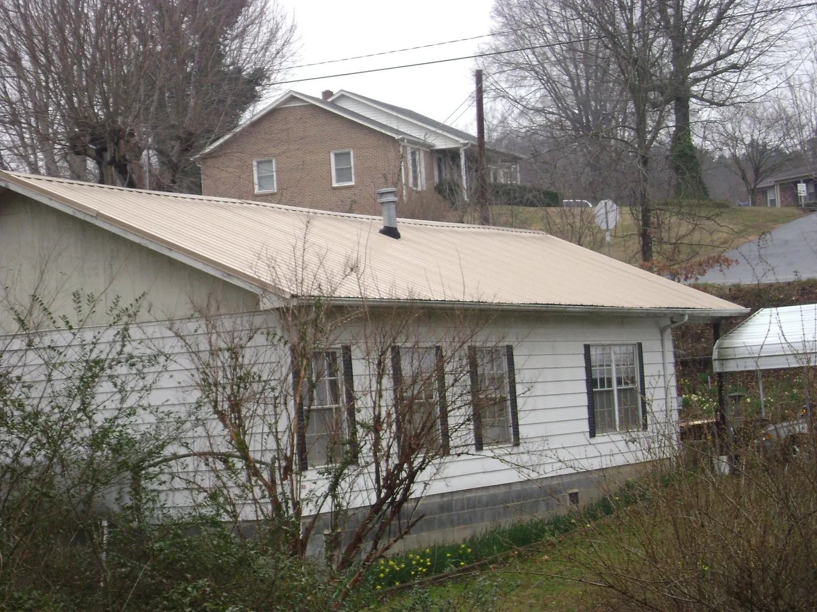 Tan metal roof on a white sided house set into a hillside — Commercial Roofing by Roofing Brothers in Sherburne