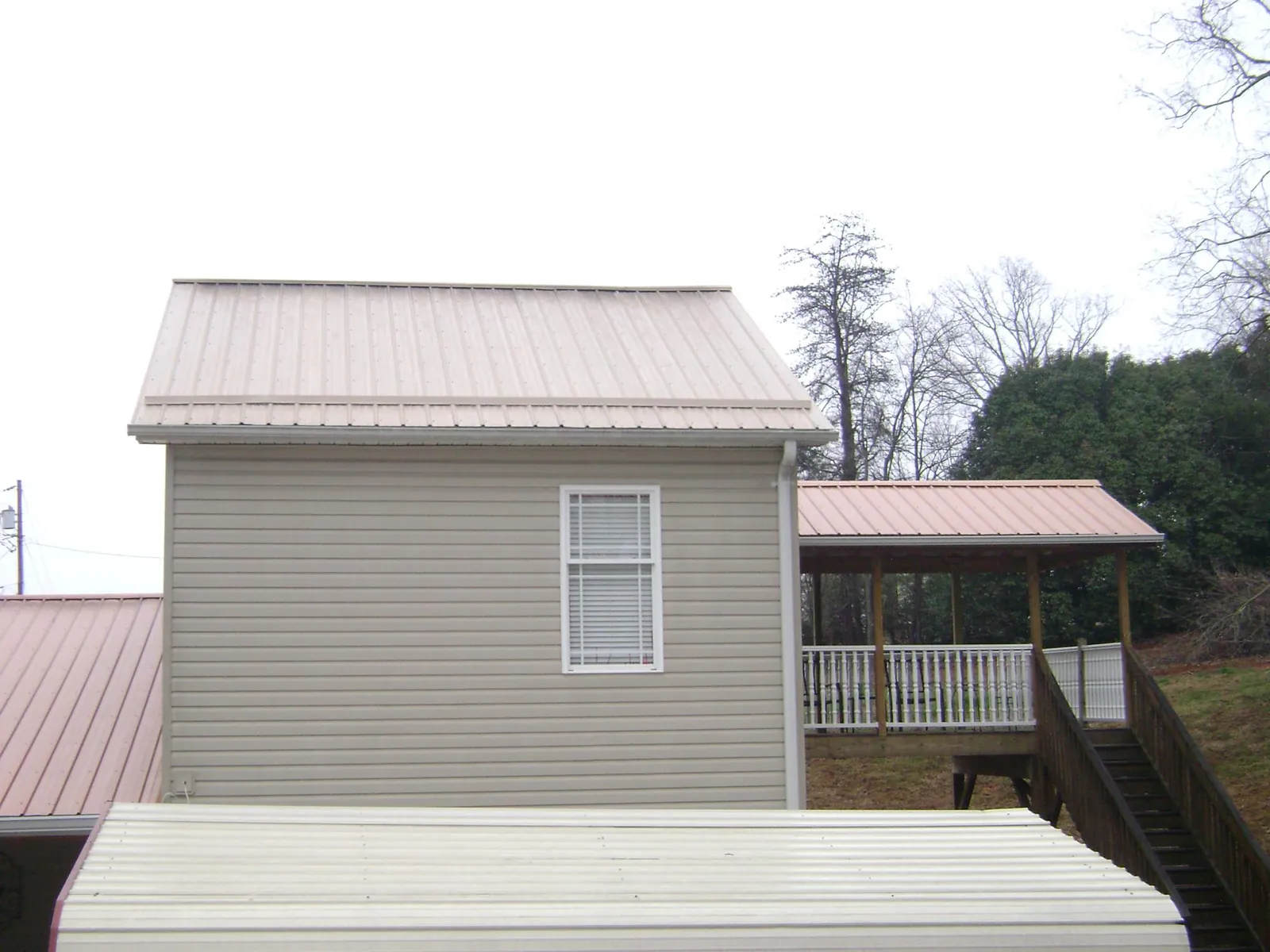 Tan metal roofs on a two story addition and attached porch, from a Roof Replacement job in Sherburne
