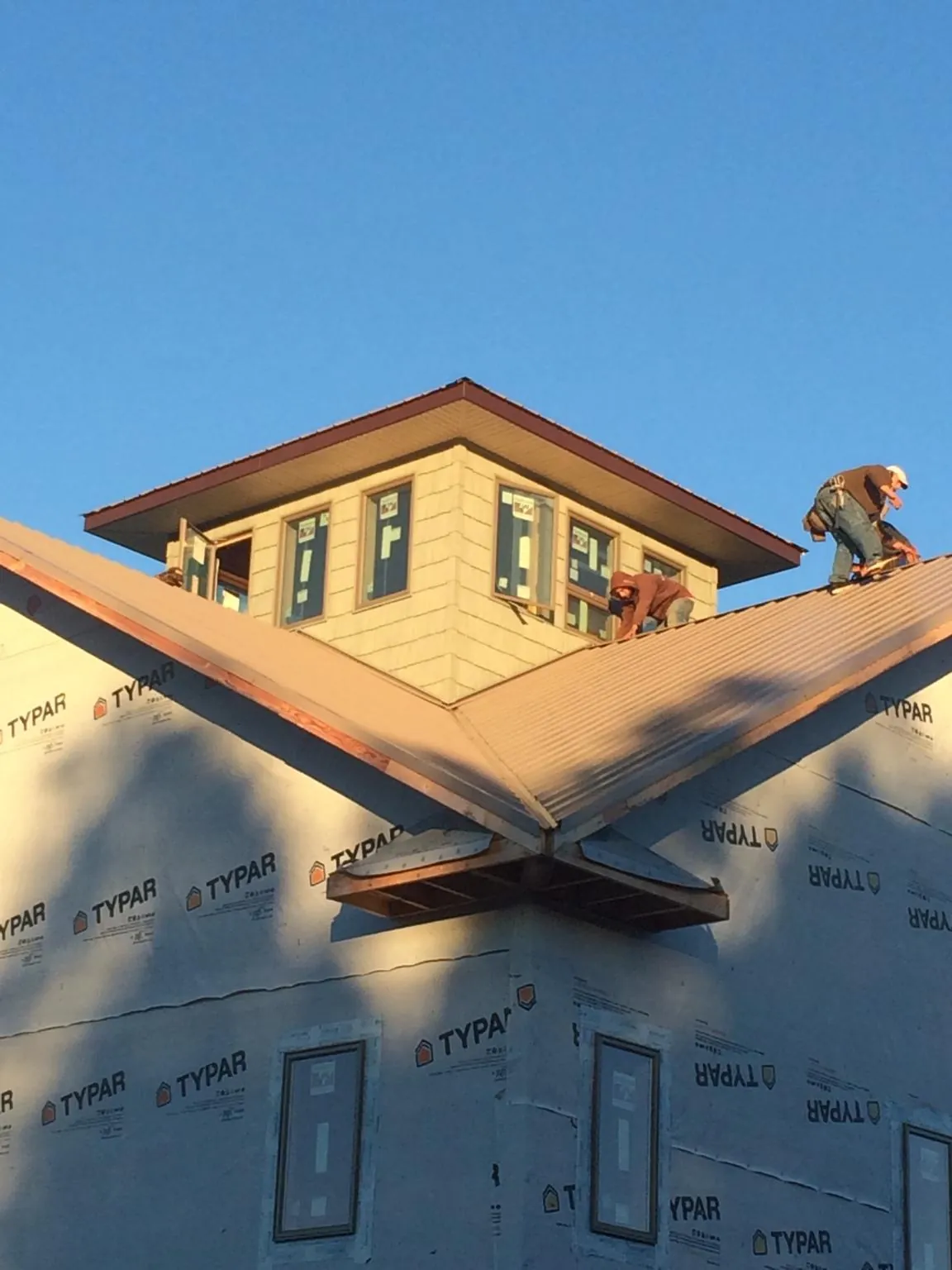 Roofers working around a rooftop cupola on a new metal roof at sunset — Roof Waterproofing in Sherburne by Roofing Brothers